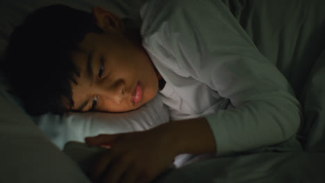 Young-Boy-In-Bedroom-At-Home-Lying-In-Bed-Using-Mobile-Phone-To-Text-Message-At-Night-4